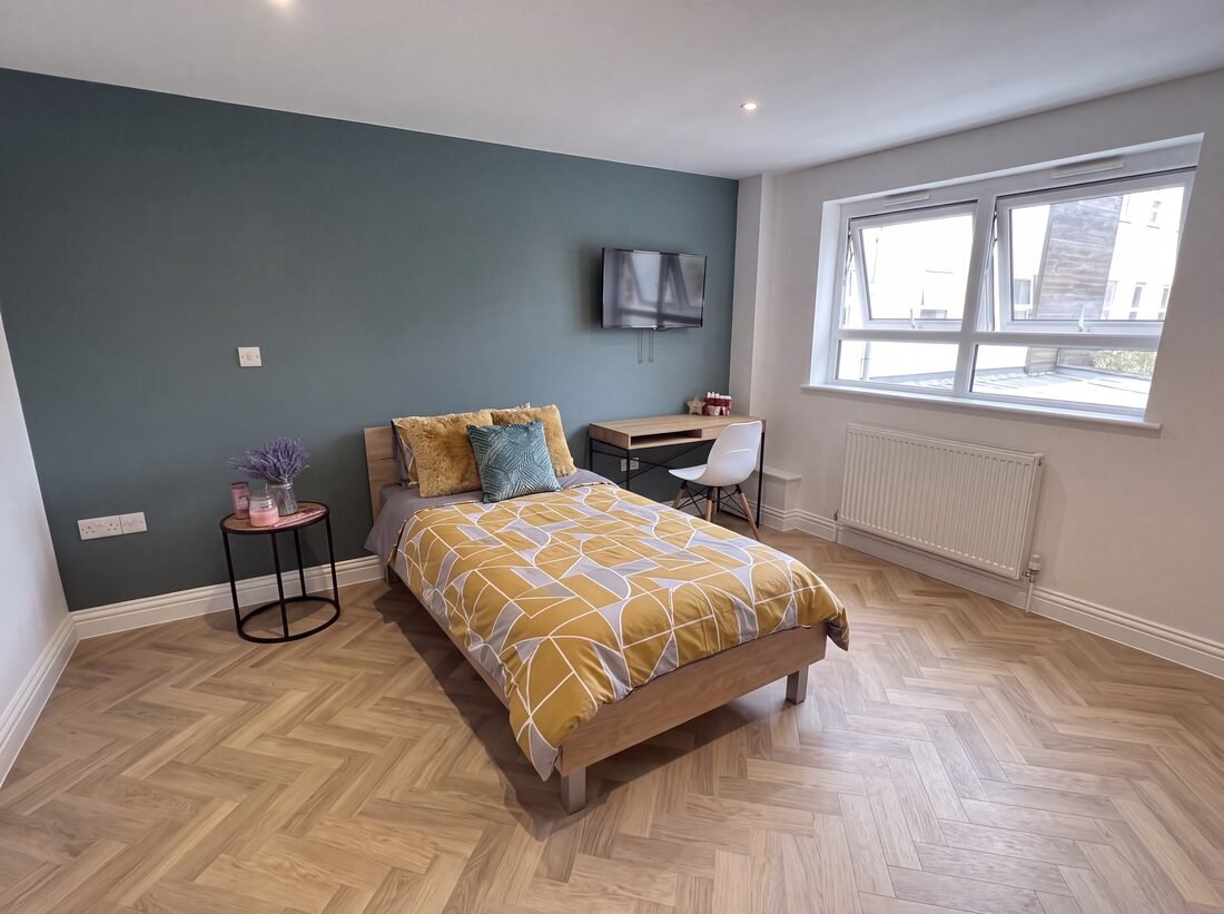 En-suite room with a single bed, teal feature wall, desk and wall-mounted TV